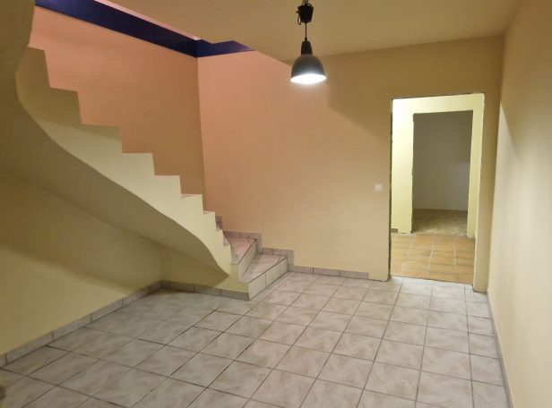 Raum mit Treppe, gelben Wänden und einem offenen Durchgang zu einem weiteren Zimmer.