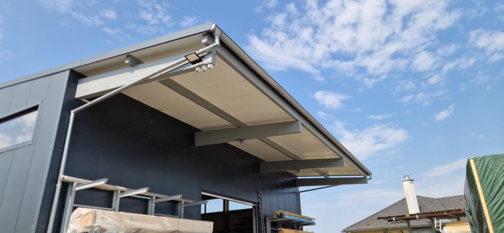 Dach eines modernen Gebäudes mit blauen Wänden und wolkigem Himmel im Hintergrund.